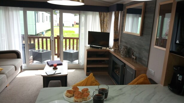 A cozy living room with a sofa, a coffee table, a TV, and a fireplace. - Lovely 2-bedroom Lodge set in Beautiful Norfolk (Great Yarmouth)