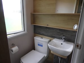 A compact bathroom with a toilet, sink, and wooden shelves. - Lovely 2-bedroom Lodge set in Beautiful Norfolk (Great Yarmouth)