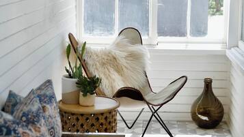 A cozy corner with a white cushioned bench, a patterned pillow, a small round table with a plant, a fluffy chair, and a vase.
