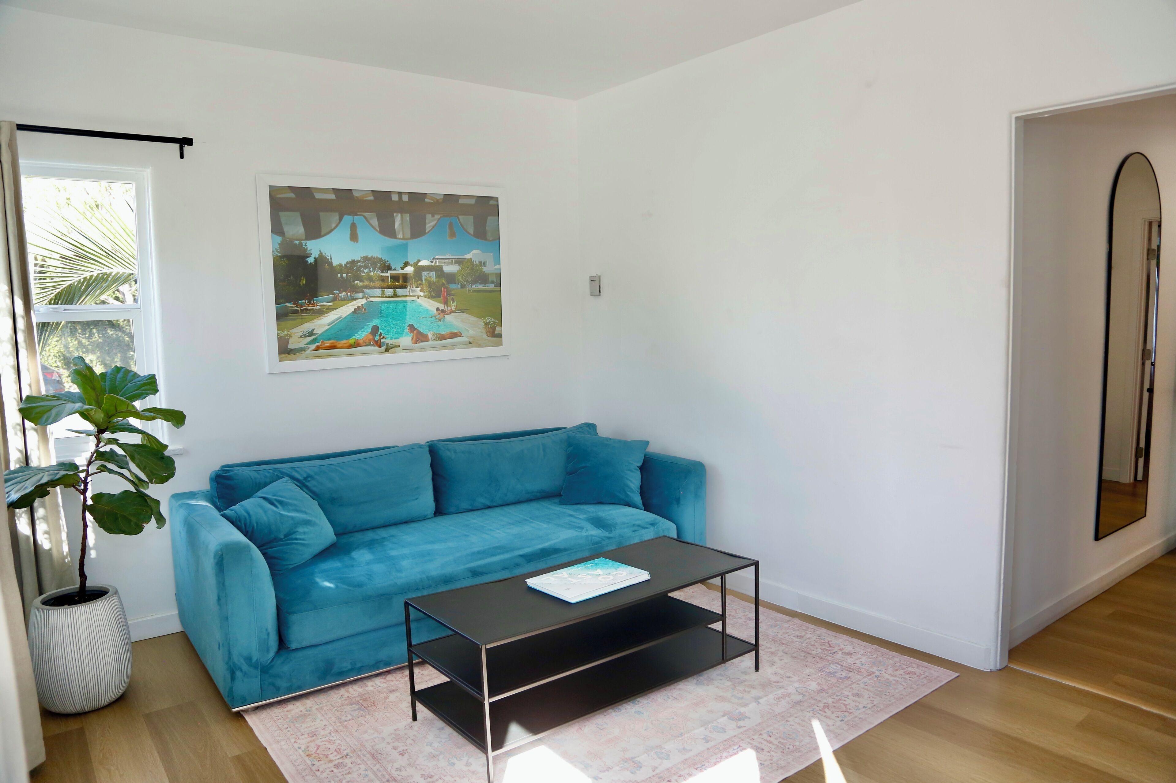 A living room with a blue sofa, a coffee table, a large framed picture, and a potted plant.