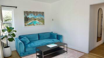 A living room with a blue sofa, a coffee table, a large framed picture, and a potted plant.