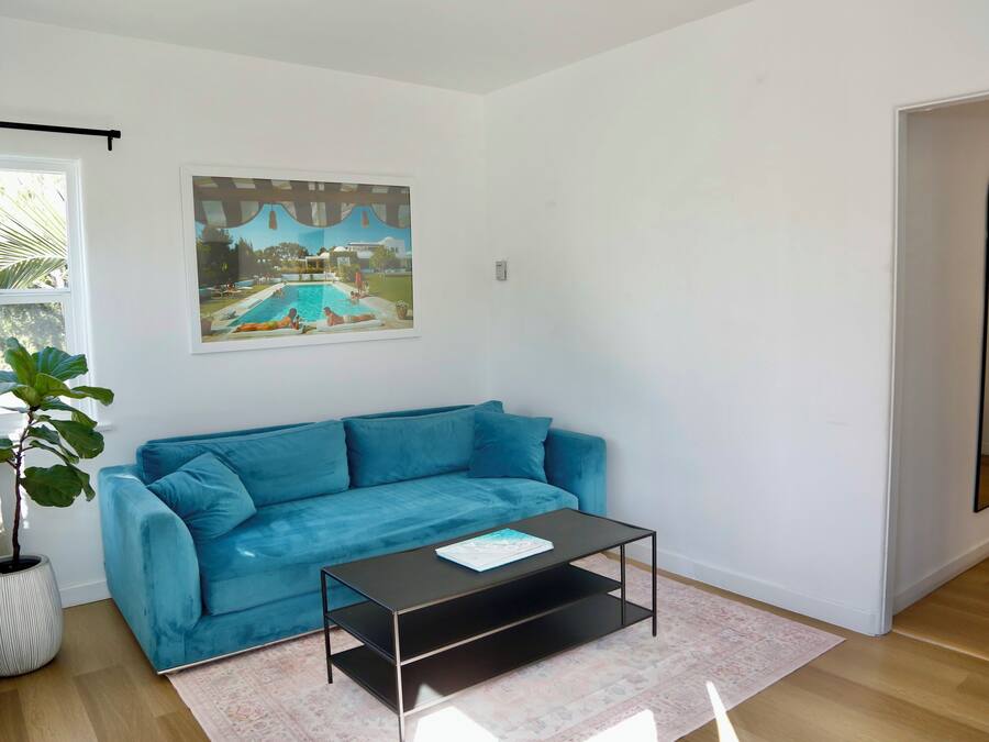 A living room with a blue sofa, a coffee table, a large framed picture, and a potted plant.
