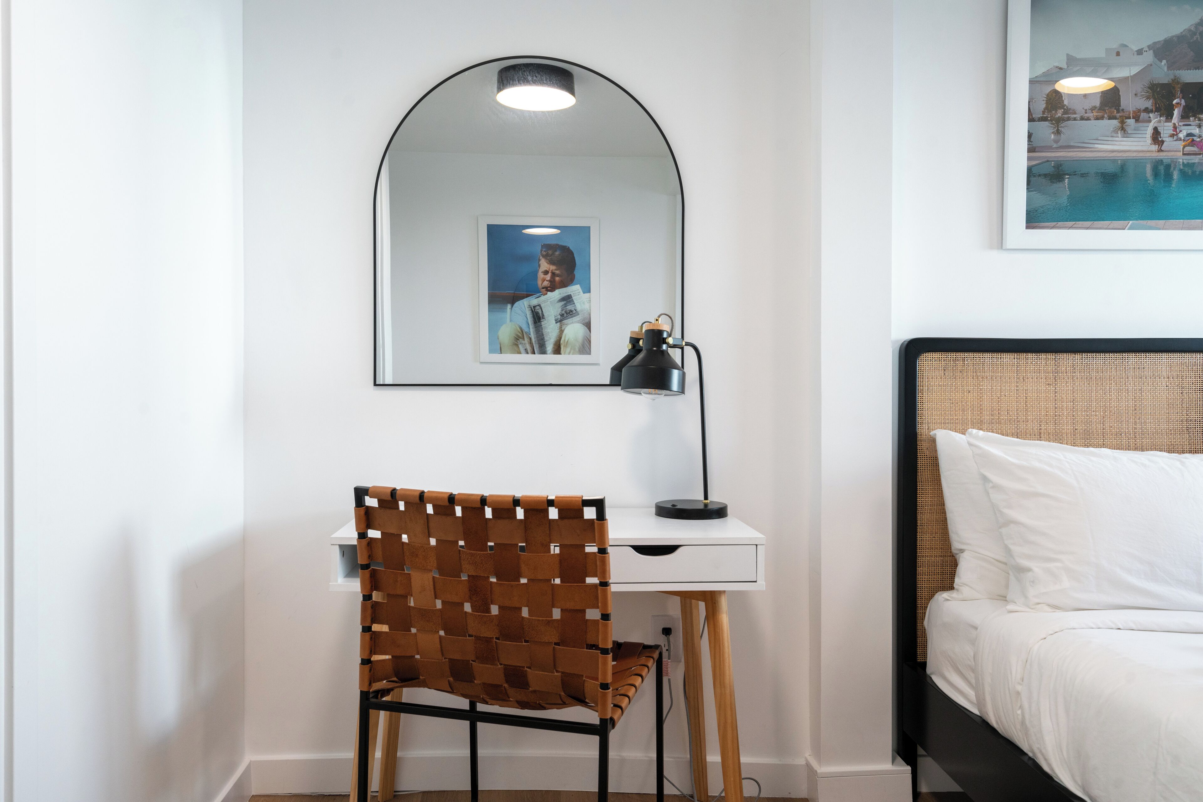 A bedroom with a bed, a desk with a chair, a mirror, and a framed picture on the wall.
