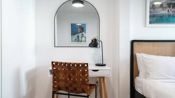 A bedroom with a bed, a desk with a chair, a mirror, and a framed picture on the wall.