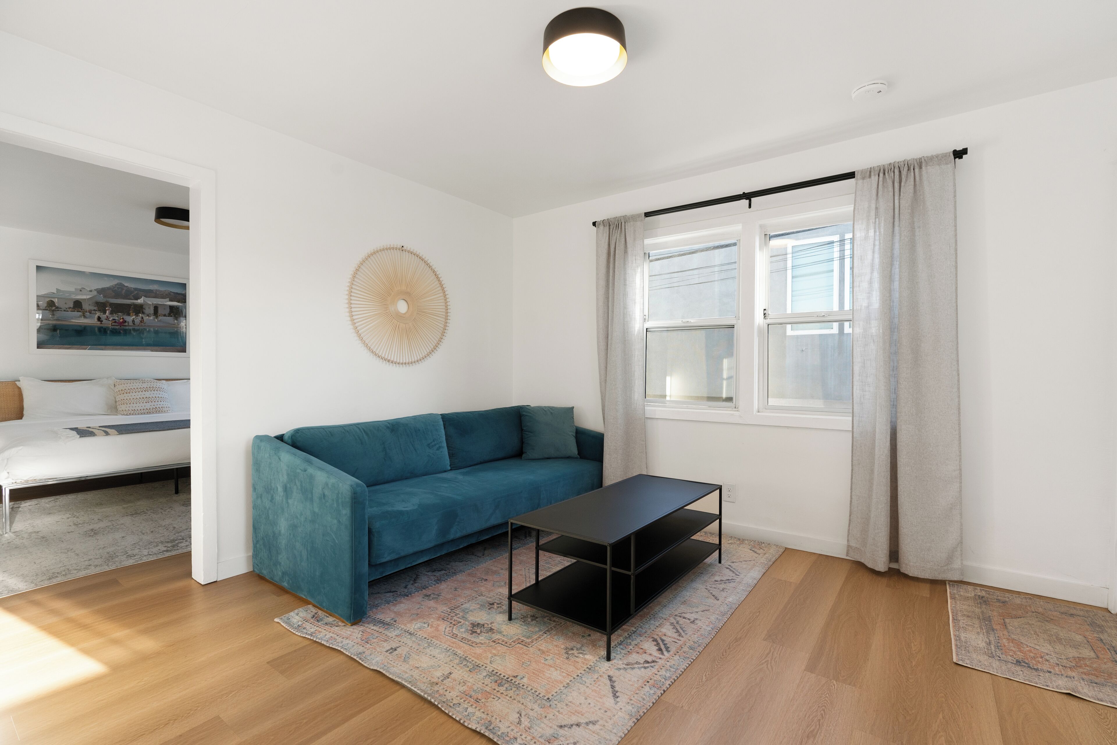 Uma sala de estar moderna com um sofá azul-turquesa, uma mesa de centro preta e uma janela grande com cortinas.