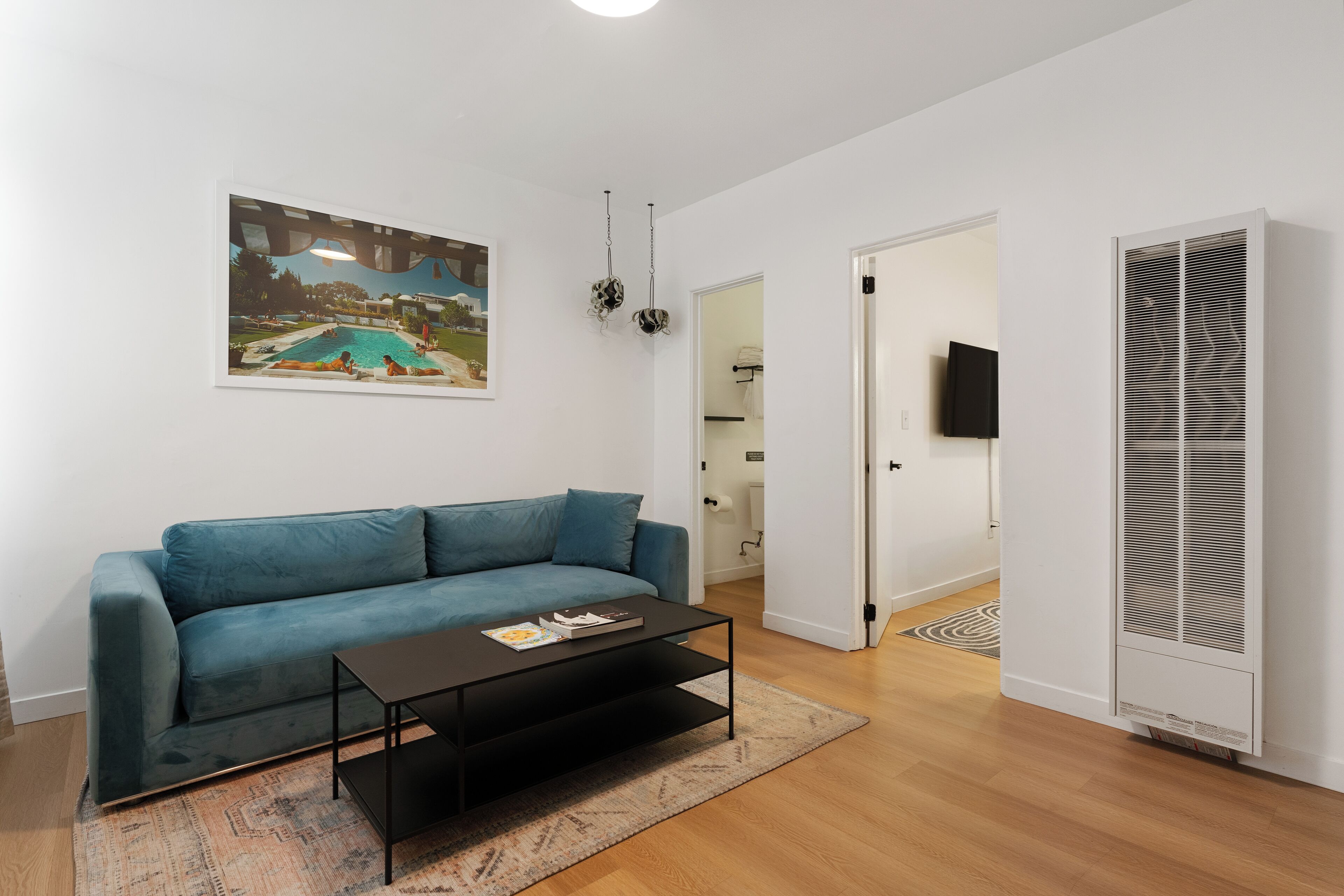A living room with a blue sofa, a coffee table, a painting of a pool, and a white wall.