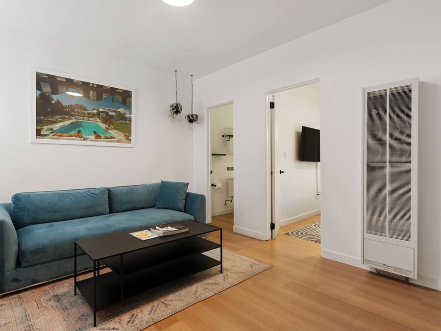 A living room with a blue sofa, a coffee table, a painting of a pool, and a white wall.