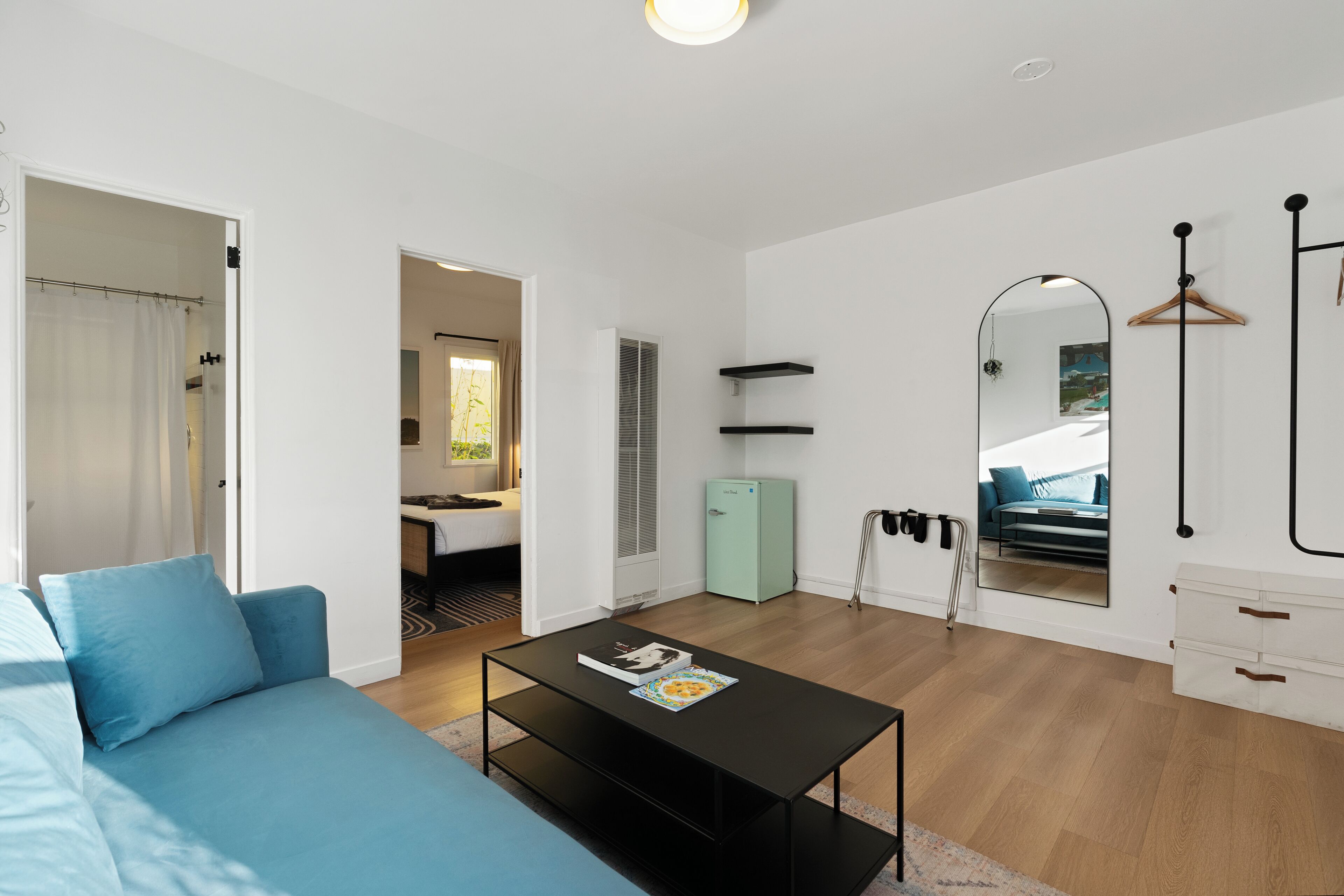 Un salon moderne avec un canapé bleu, une table basse noire et une petite cuisine intégrée.