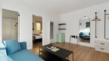 Un salon moderne avec un canapé bleu, une table basse noire et une petite cuisine intégrée.