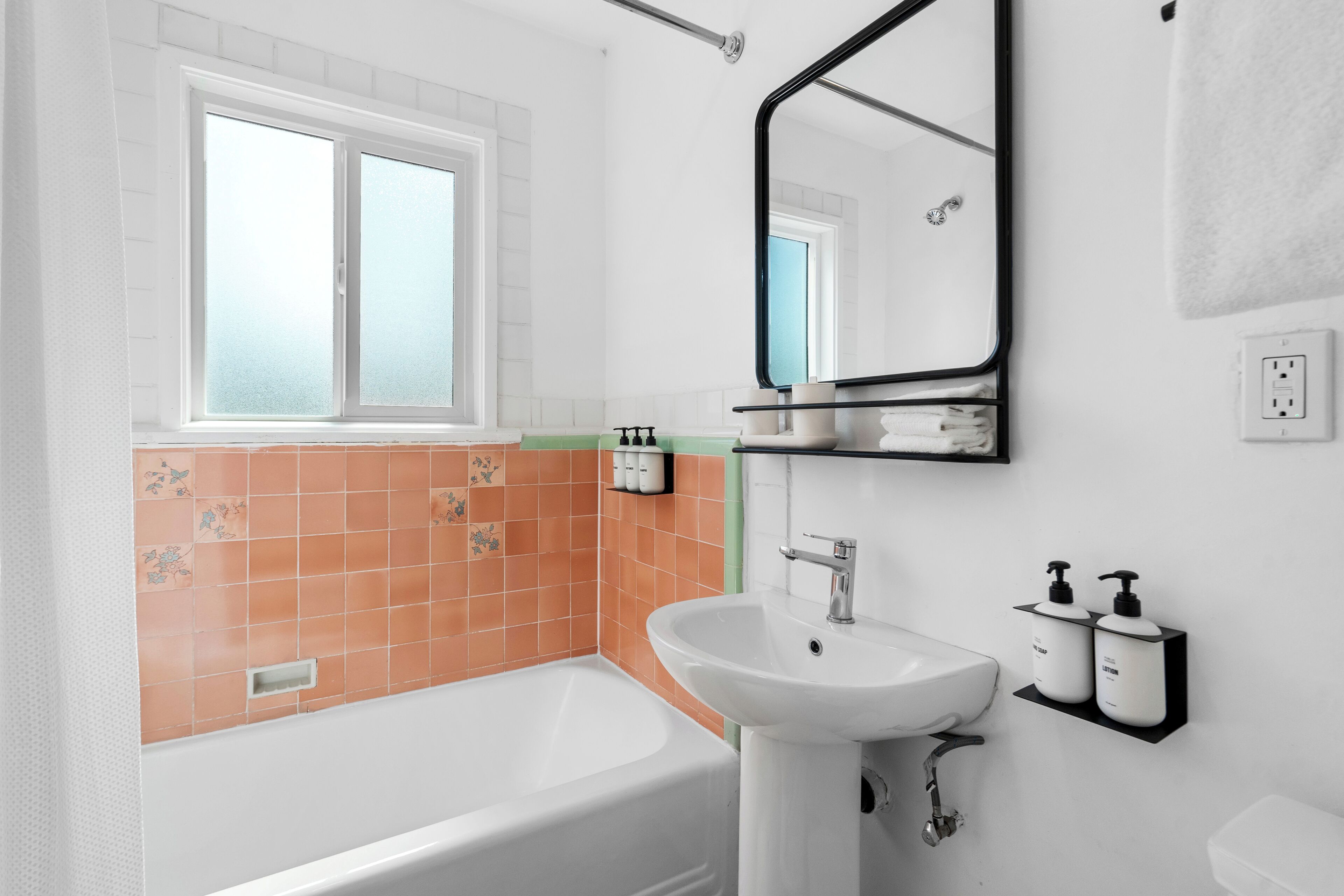 Une salle de bain avec une baignoire blanche, un lavabo blanc et un miroir au-dessus du lavabo. Il y a une fenêtre avec du verre dépoli et un porte-serviettes fixé au mur.