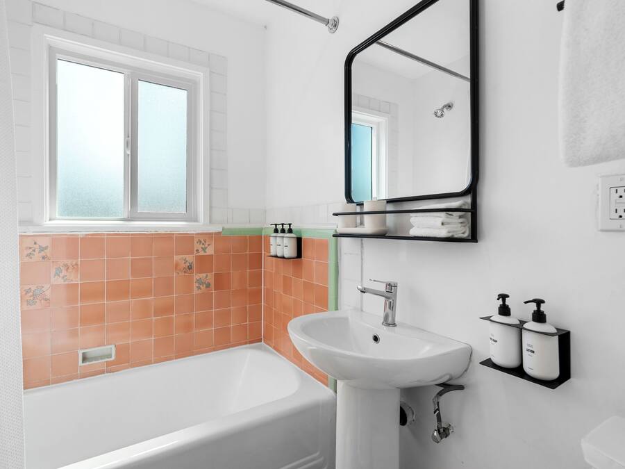 Une salle de bain avec une baignoire blanche, un lavabo blanc et un miroir au-dessus du lavabo. Il y a une fenêtre avec du verre dépoli et un porte-serviettes fixé au mur.