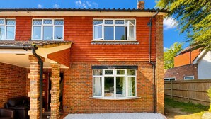 A two-story house with a brick exterior, a covered patio area, and a small front yard. - High Trees Gatwick Guest House  (Horley)