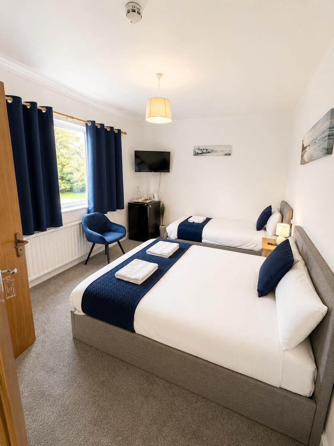 Une chambre d’hôtel avec deux lits, un bureau, une chaise, une télévision et une fenêtre avec des rideaux.
