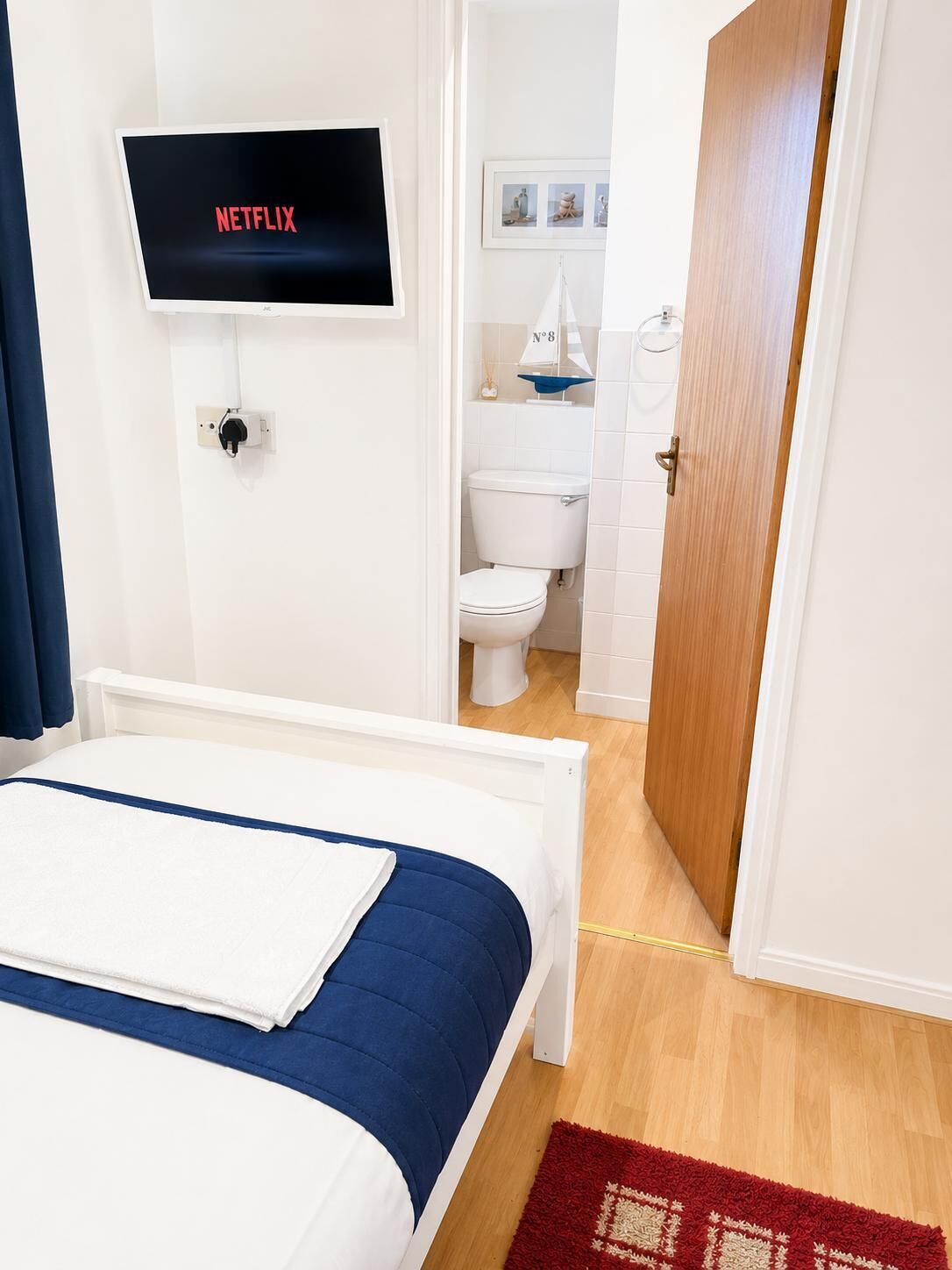 A hotel room with a bed, a television mounted on the wall, a bathroom with a toilet and sink, and a wooden door.
