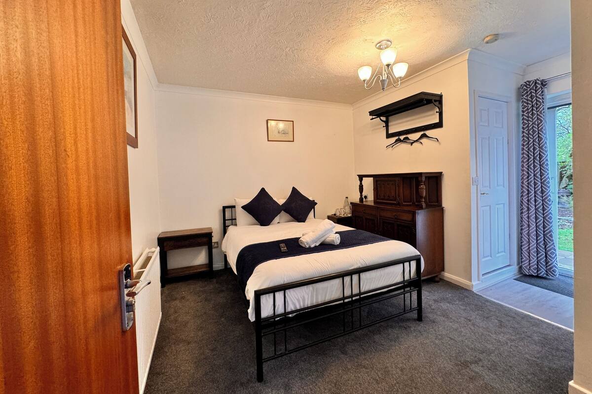 A bedroom with a bed, bedside tables, a nightstand, a dresser, a hanging light fixture, and a door leading to a balcony.
