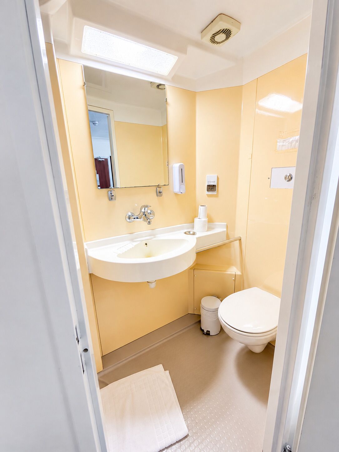 A compact bathroom with a sink, mirror, toilet, and a towel on the floor.