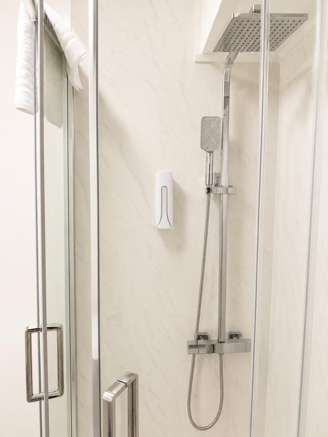 A modern shower enclosure with a handheld showerhead, a wall-mounted control panel, and a glass door with a towel hanging on the handle.