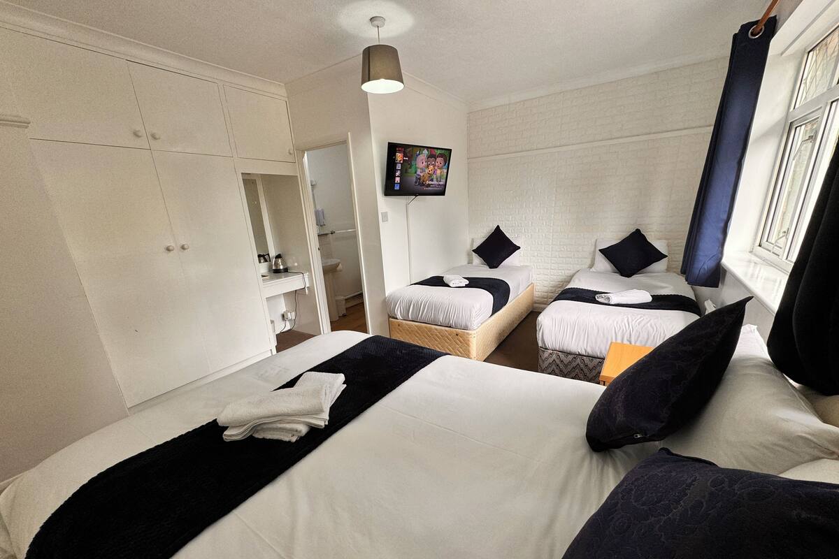 A hotel room with two beds, a flat-screen TV mounted on the wall, and a window with curtains.