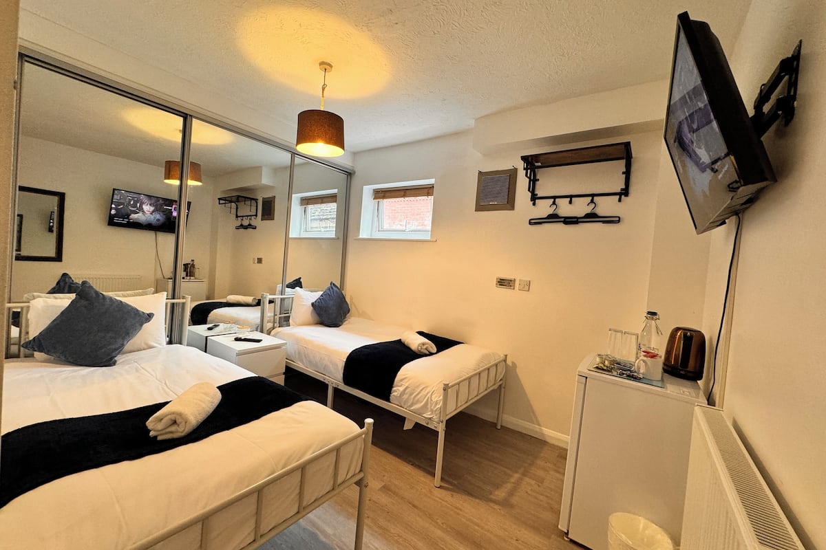 A hotel room with two beds, a TV, a mirror, a heater, and a small table with a kettle.