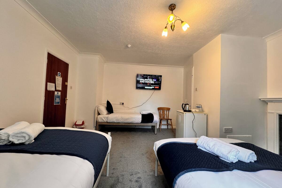 A hotel room with two beds, a desk with a kettle, a TV, and a fireplace.