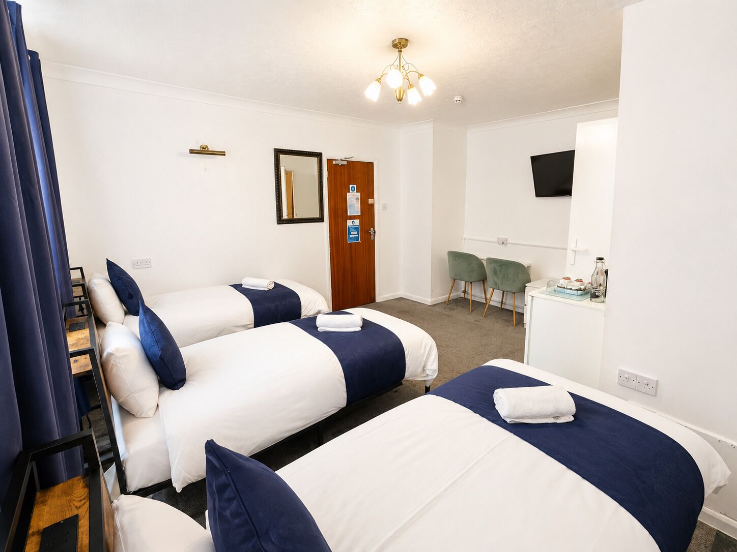 A hotel room with two beds, a desk, a chair, a television, and a door.