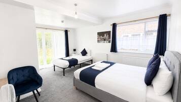 A modern hotel room with a large bed, a smaller bed, a chair, a bedside table, and a view of the city.
