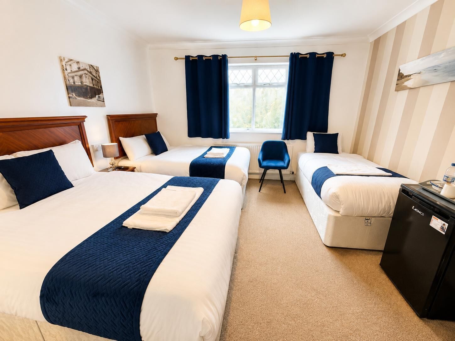 A hotel room with two beds, a small table, a chair, and a desk with a computer.