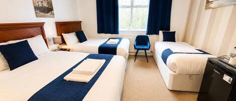 A hotel room with two beds, a small table, a chair, and a desk with a computer.