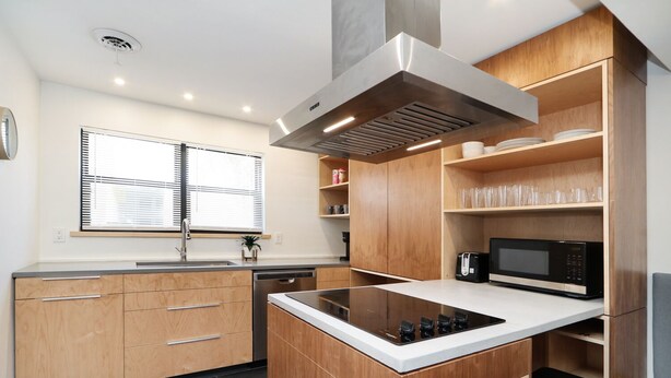 Una cucina moderna con mobili in legno, una cappa aspirante in acciaio inossidabile, un forno a microonde e un'isola integrata con piano cottura.