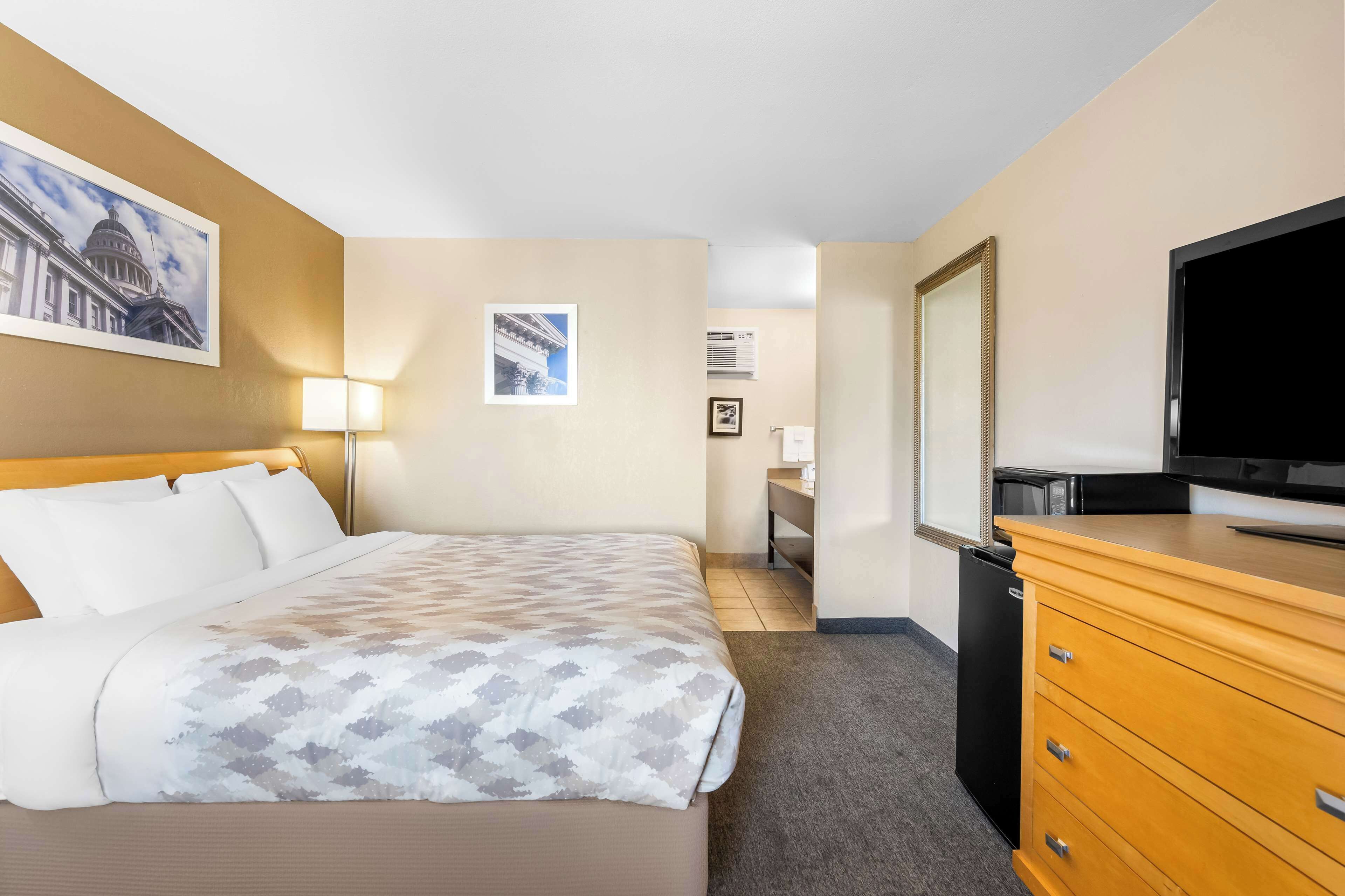 A hotel room with a bed, a dresser, a television, and a desk with a chair.