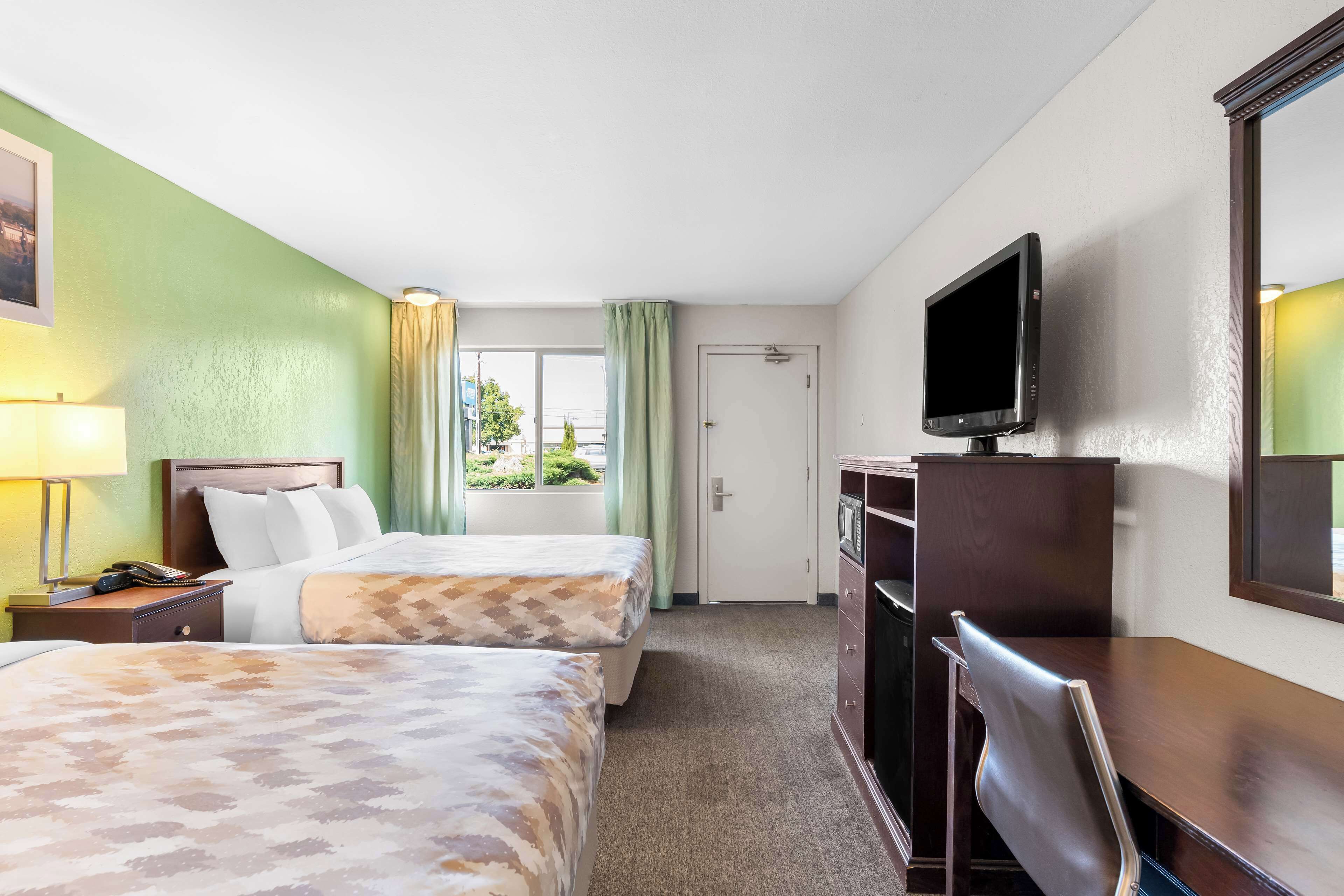 A hotel room with two beds, a desk, a TV, and a window with curtains.