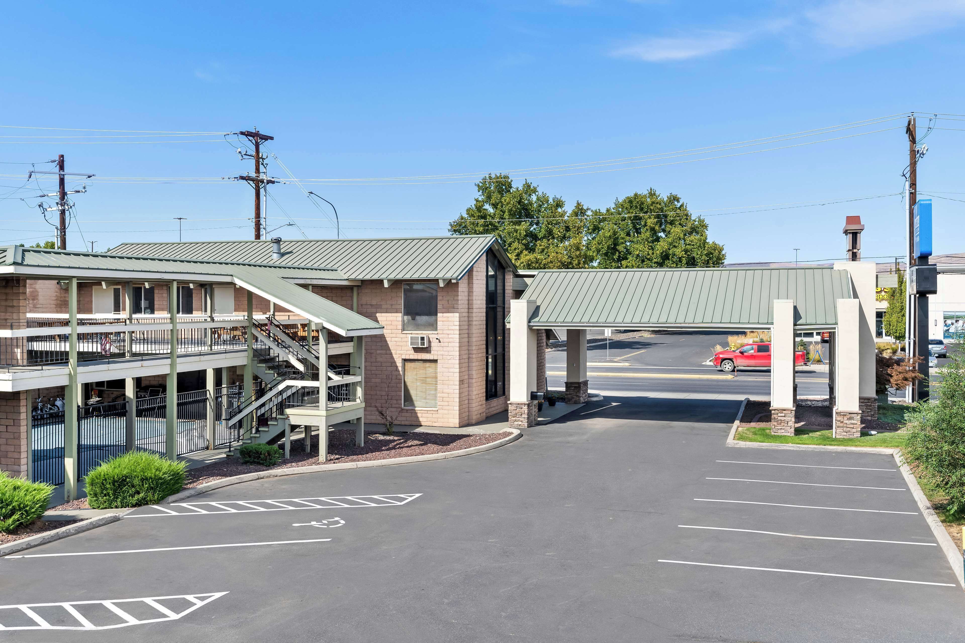 A parking lot with a covered walkway leading to a building with a brick facade and a green roof.
