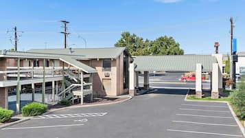 A parking lot with a covered walkway leading to a building with a brick facade and a green roof.