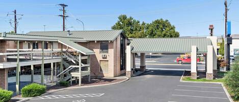 A parking lot with a covered walkway leading to a building with a brick facade and a green roof.
