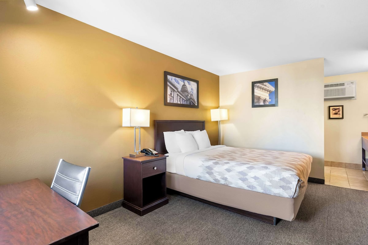A hotel room with a bed, a desk, two lamps, and a nightstand.