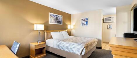 A hotel room with a bed, bedside tables, a desk, and a chair. There are wall-mounted lamps and framed pictures on the walls.
