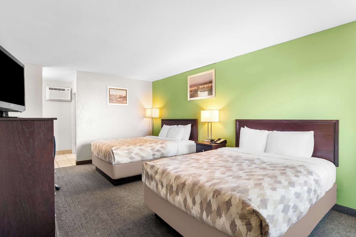 A hotel room with two beds, a desk, a TV, and a green accent wall.