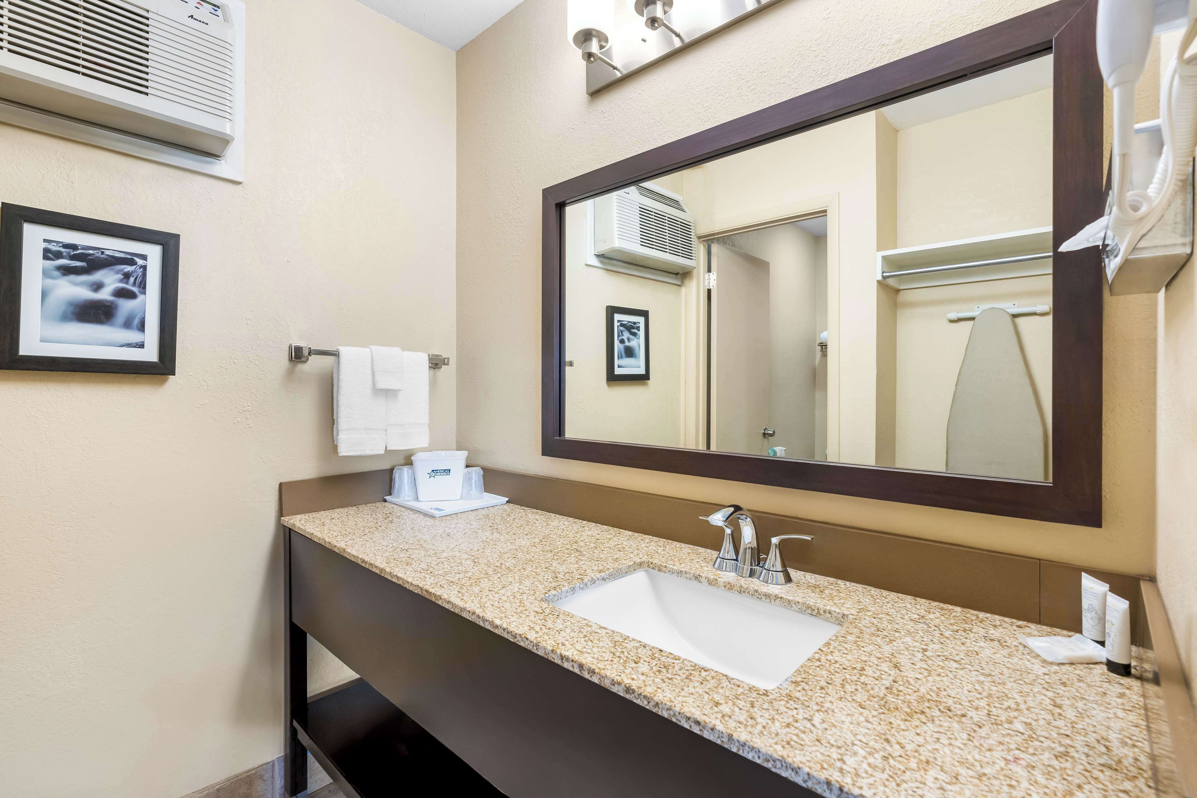 Un baño de hotel con lavamanos de encimera de granito, un espejo grande, un perchero y un cuadro en la pared.