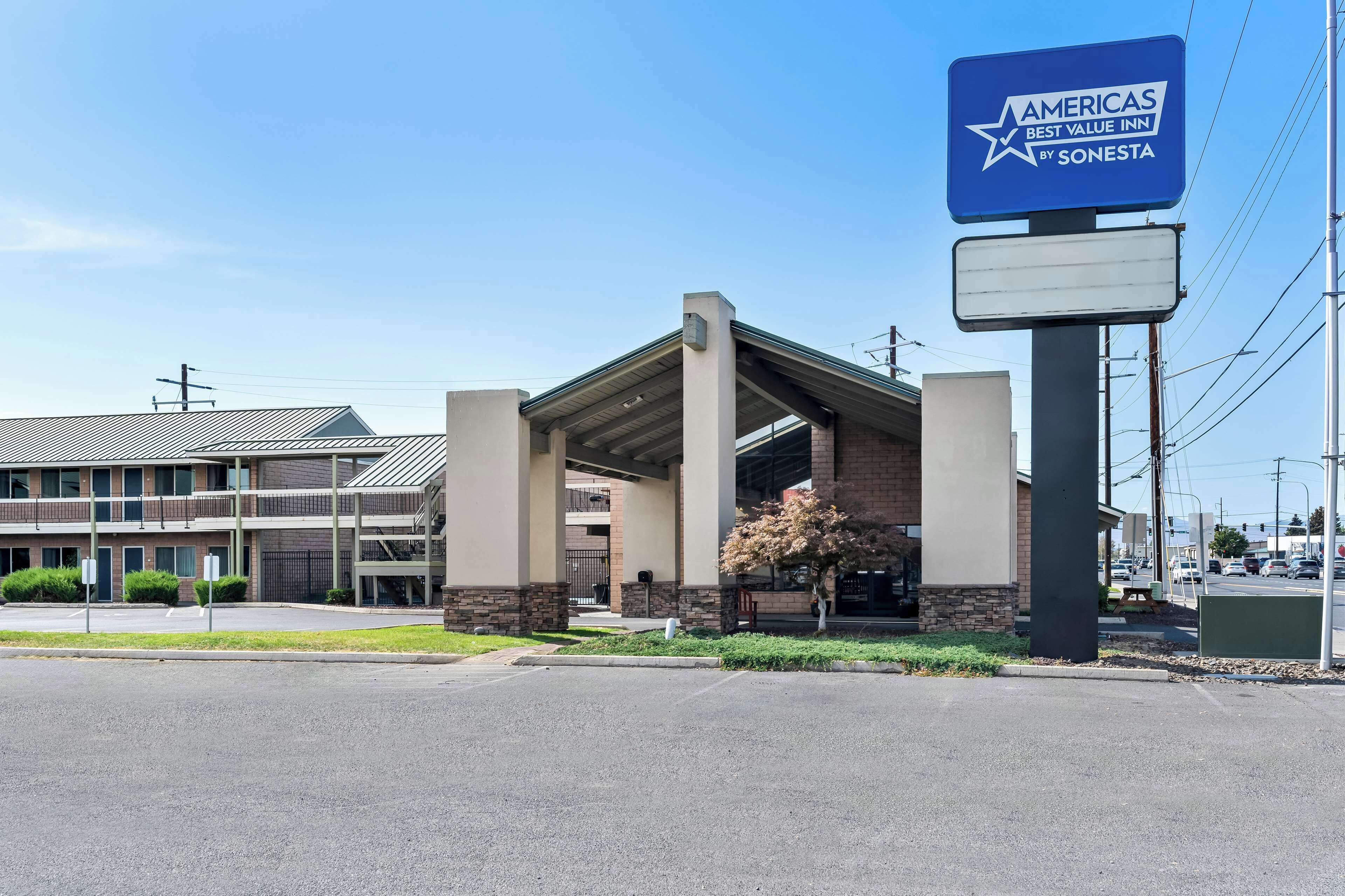 En hotellentrén med en överbyggd gångväg, en skylt med texten ”Americas Best Value Inn by Sonesta” och en parkeringsplats.