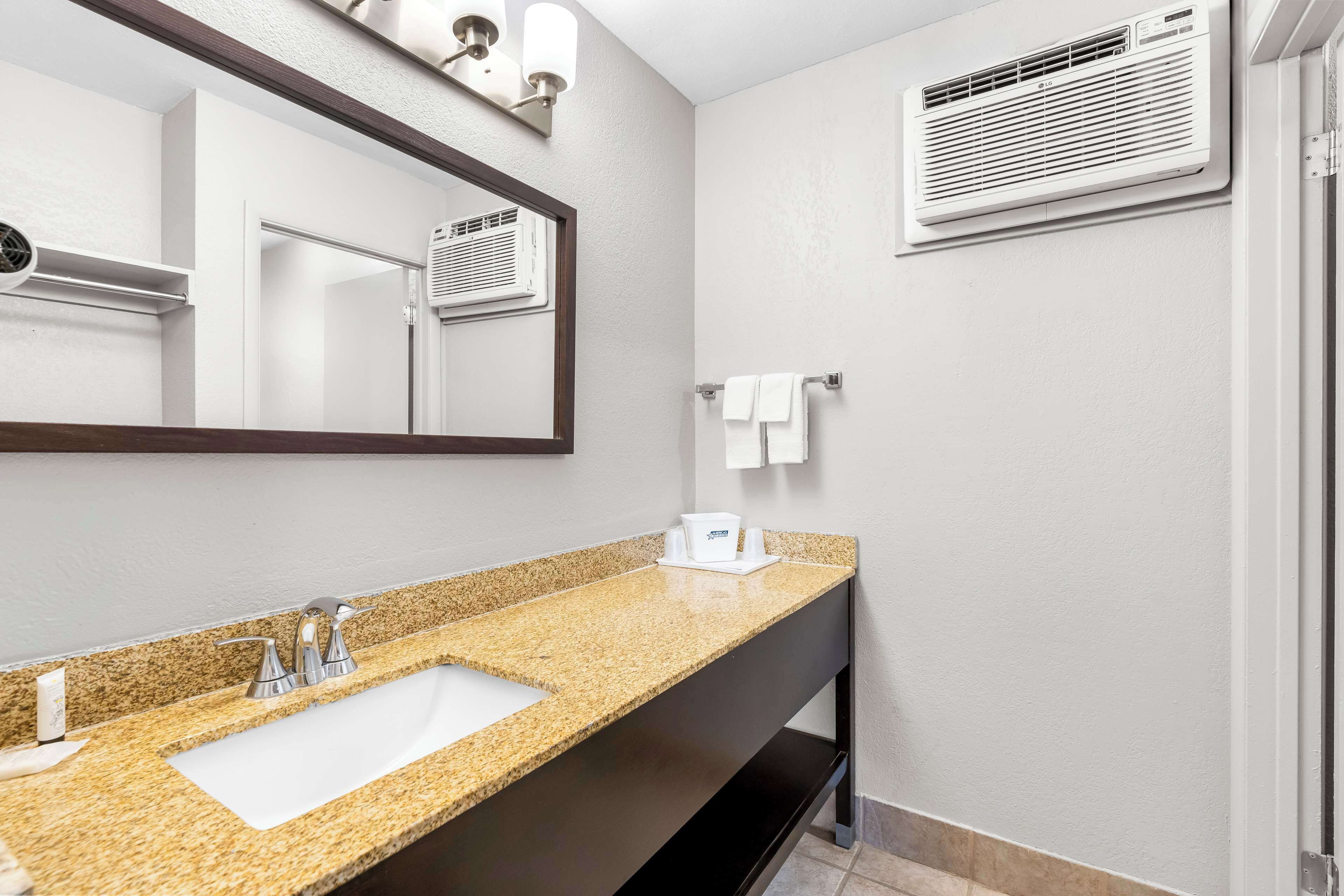 Une salle de bain moderne avec un lavabo doté d’un plan de travail en granit, un grand miroir et une bouche d’aération fixée au mur.