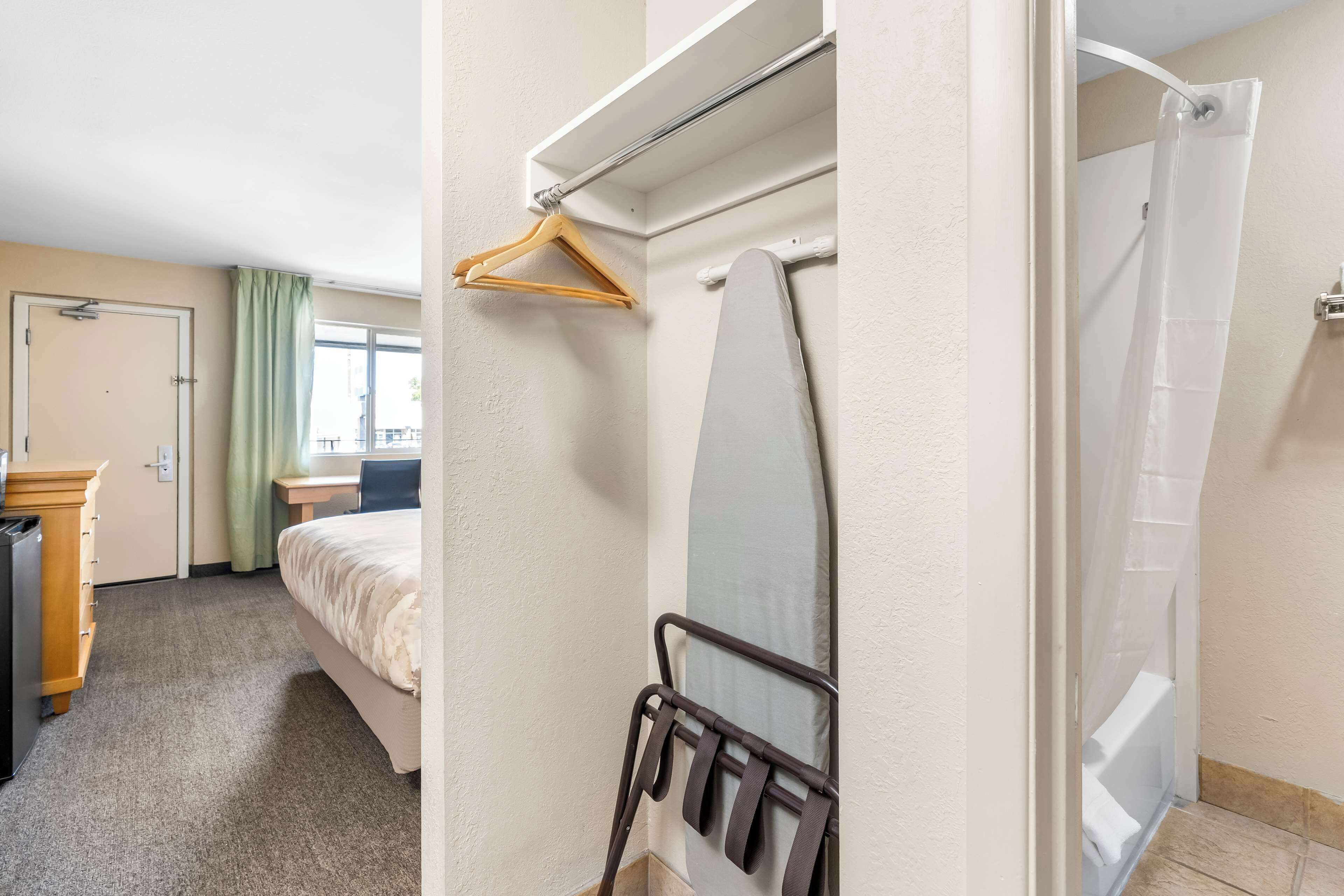 A hotel room with a bed, a desk, a hanging shower curtain, and a coat rack.