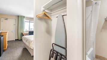 A hotel room with a bed, a desk, a hanging shower curtain, and a coat rack.