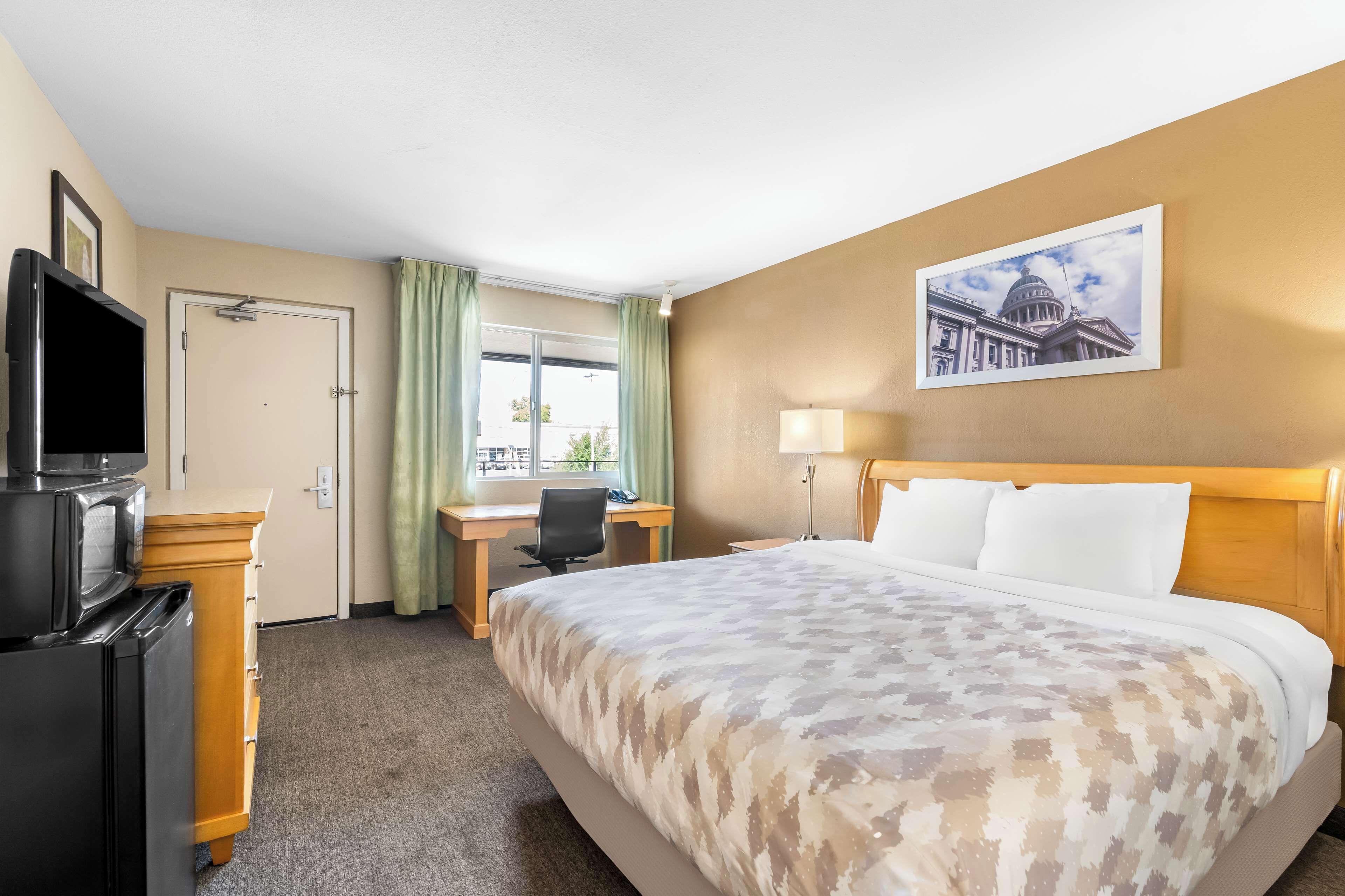 A hotel room with a bed, desk, chair, television, and a window with curtains.