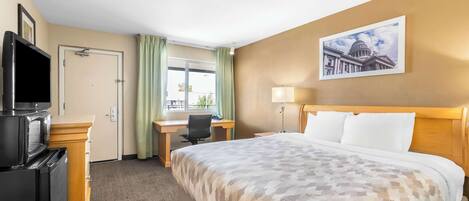 A hotel room with a bed, desk, chair, television, and a window with curtains.