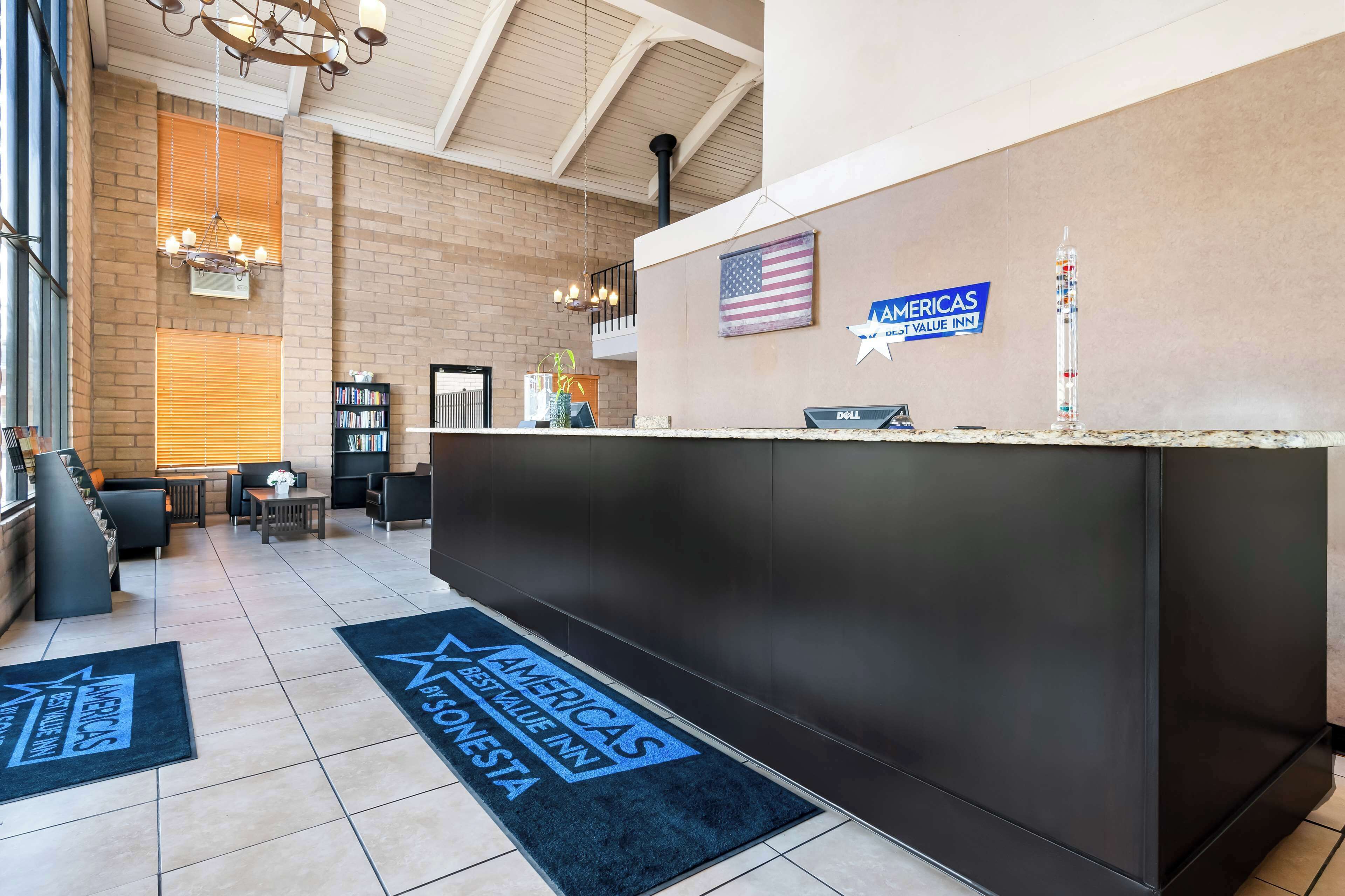 A hotel reception area with a modern design, featuring a reception desk, a flag, and a sign indicating the hotel is part of the Americas Best Value Inn chain.