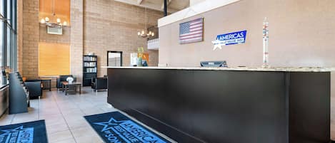 A hotel reception area with a modern design, featuring a reception desk, a flag, and a sign indicating the hotel is part of the Americas Best Value Inn chain.