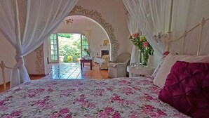 Ein Schlafzimmer mit einem großen Bett, einem Sessel, einem kleinen Tisch und Blick ins Freie.
