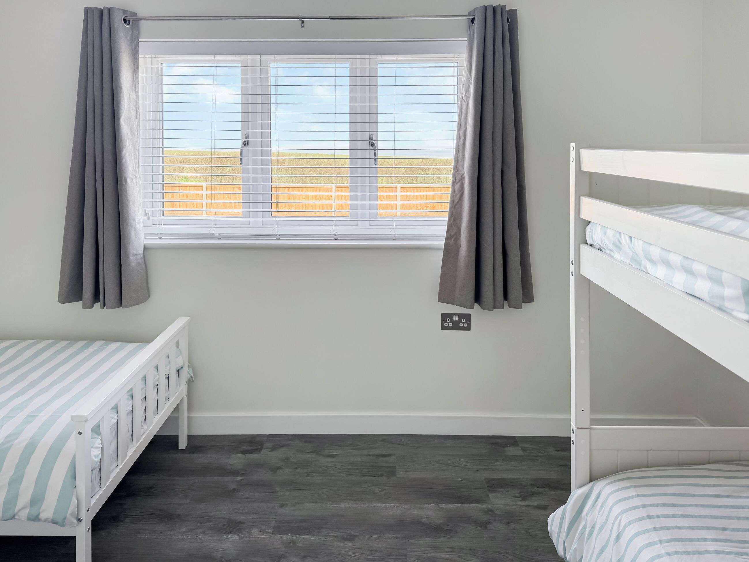 A room with a window, two bunk beds, and a power outlet on the wall.