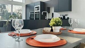 Une cuisine moderne avec des meubles de couleur sombre, une table à manger dressée avec des assiettes, des verres et une plante en pot.