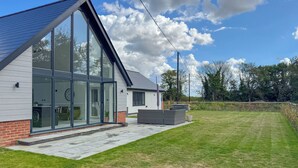 Une maison moderne dotée de grandes fenêtres en verre, d’un toit en pente et d’une pelouse bien entretenue.
